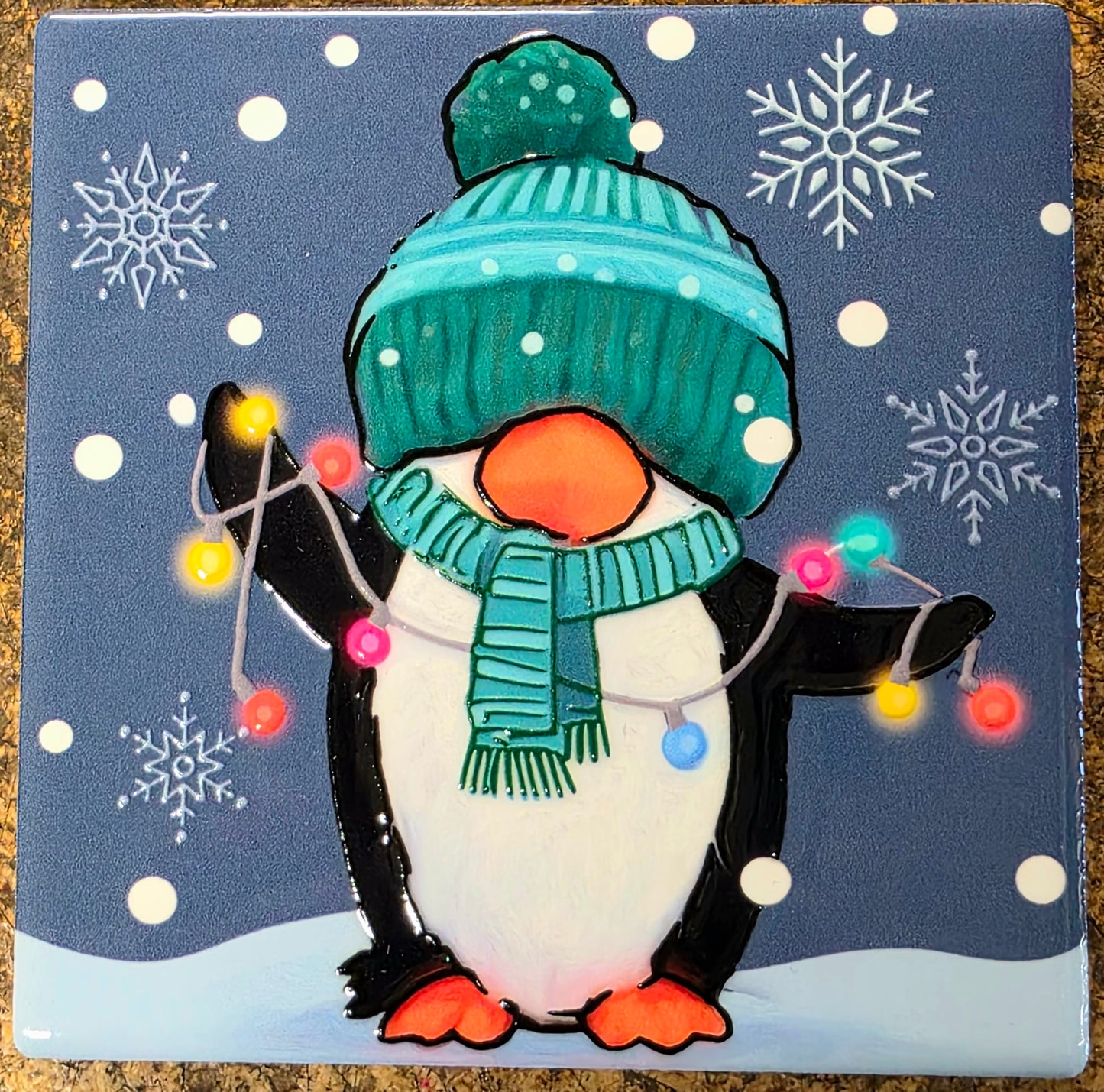 Penguin wearing a teal hat and scarf with Christmas lights against a snowy background