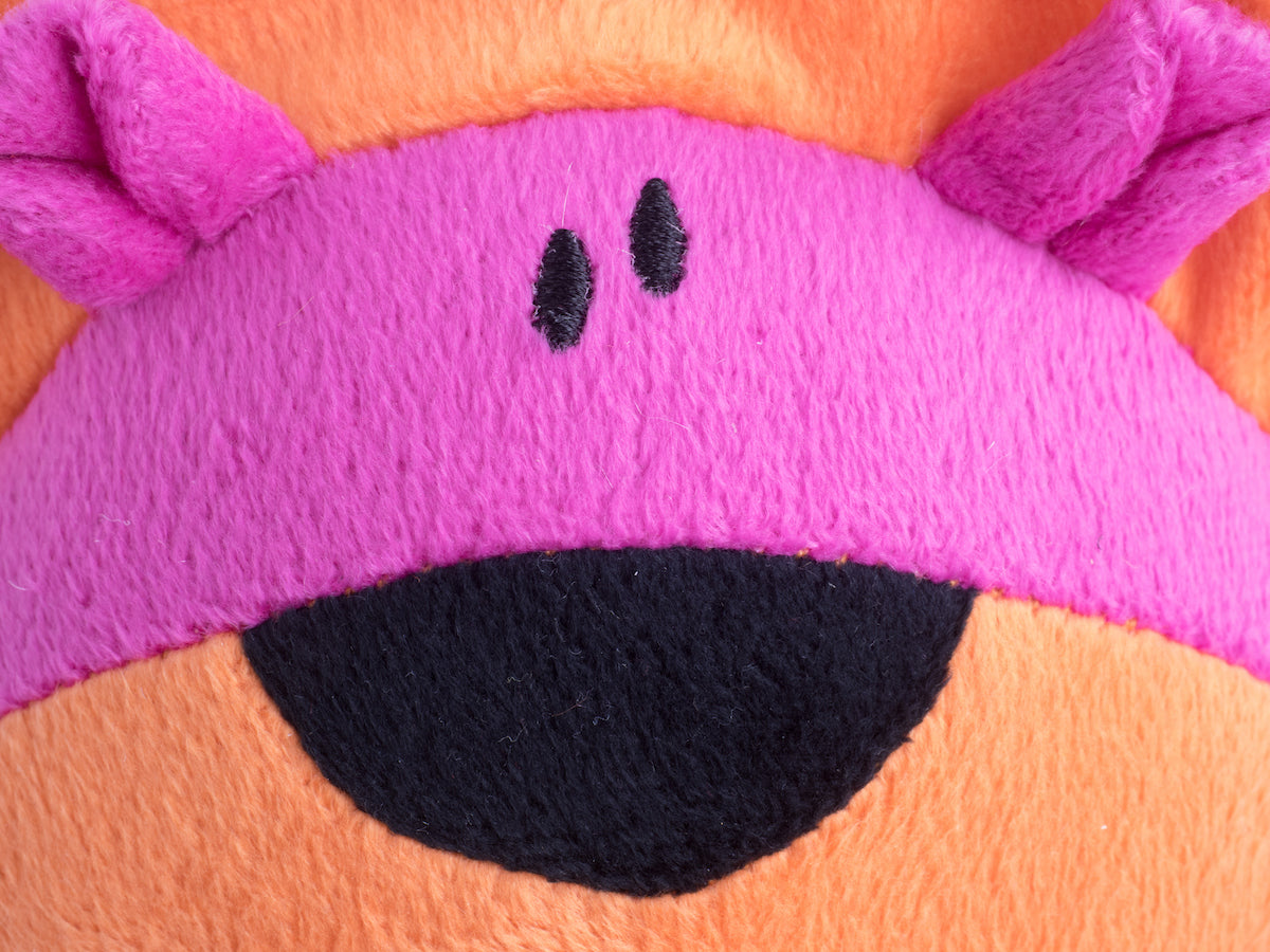 Close-up of a plush toy with a pink face and black eyes on an orange background