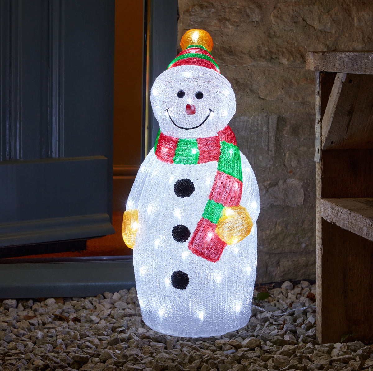 Decorative snowman light with a colorful scarf and hat on a stone surface.