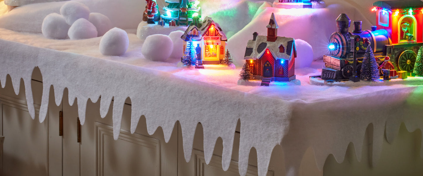 Decorative winter scene with small houses, train, and lights on a snowy platform.