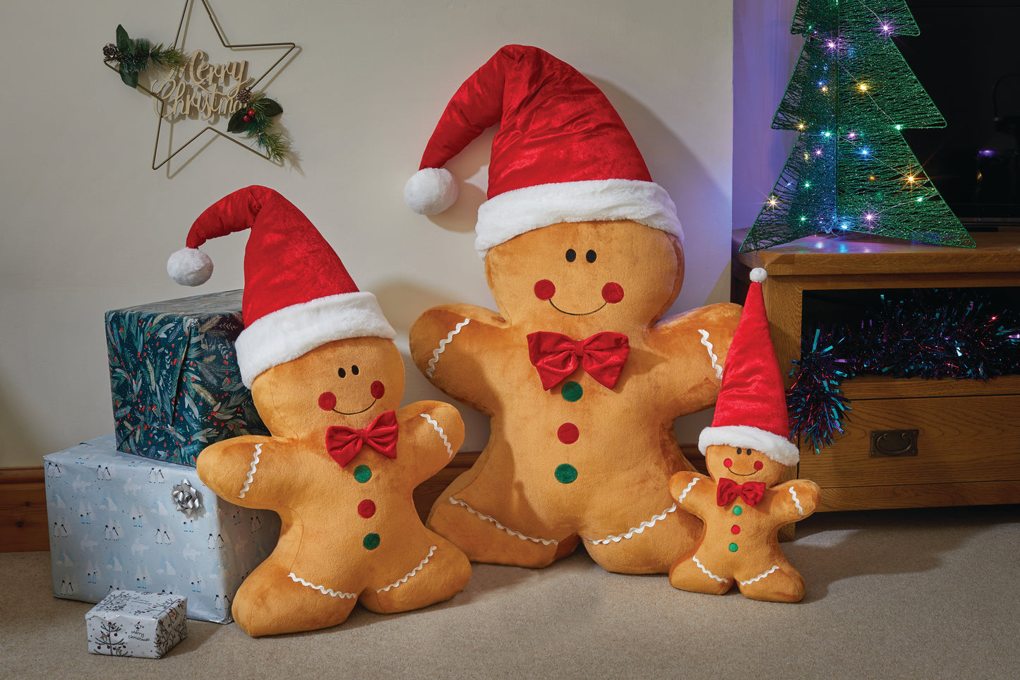 Three gingerbread men with Santa hats in front of a Christmas tree and presents.