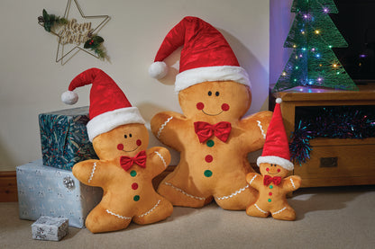 Three gingerbread men with Santa hats in front of a Christmas tree and presents.