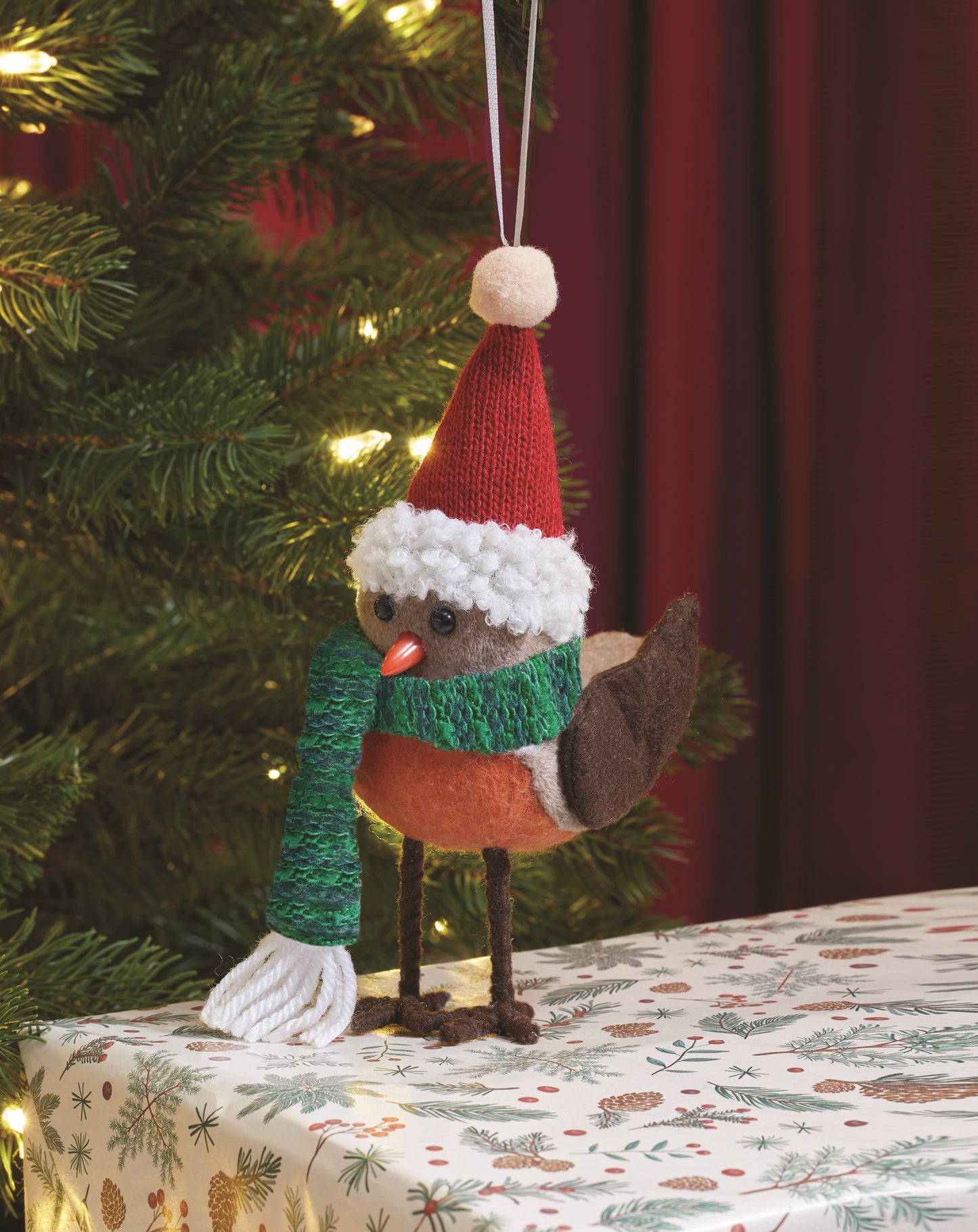 Knitted robin decoration wearing a Santa hat and scarf, hanging on a Christmas tree.