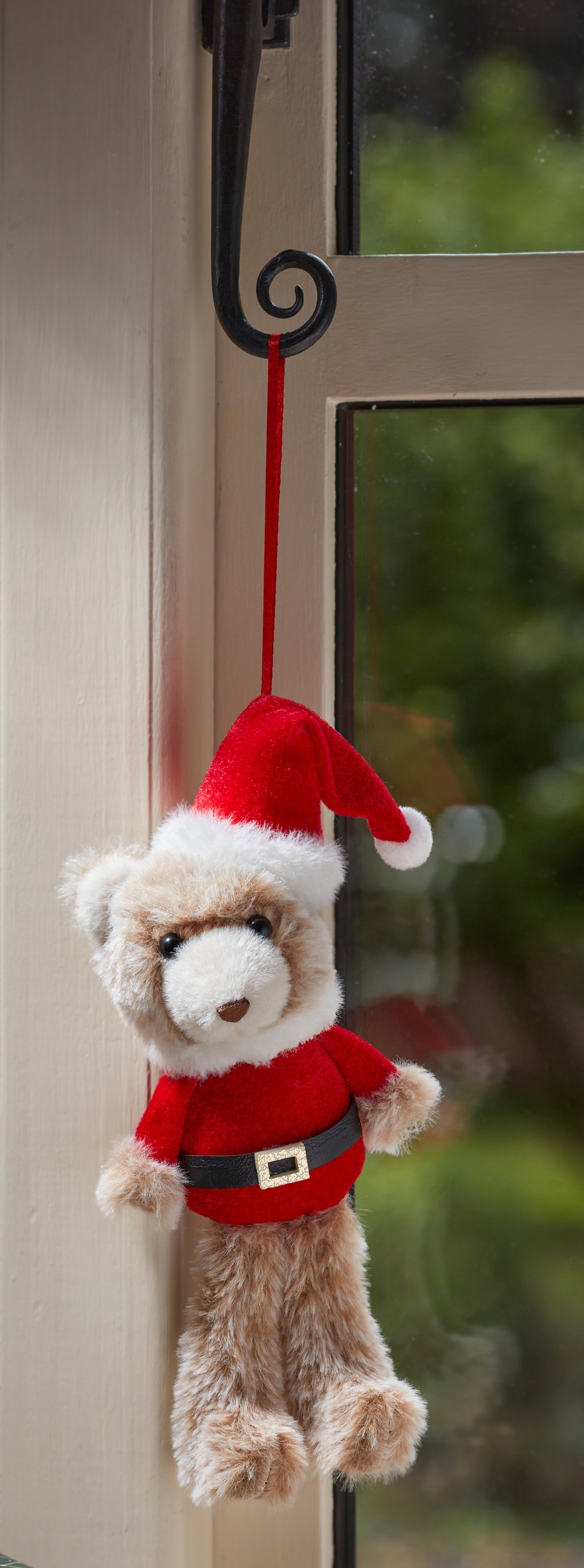 Small teddy bear wearing a Santa hat and outfit, hanging on a hook.