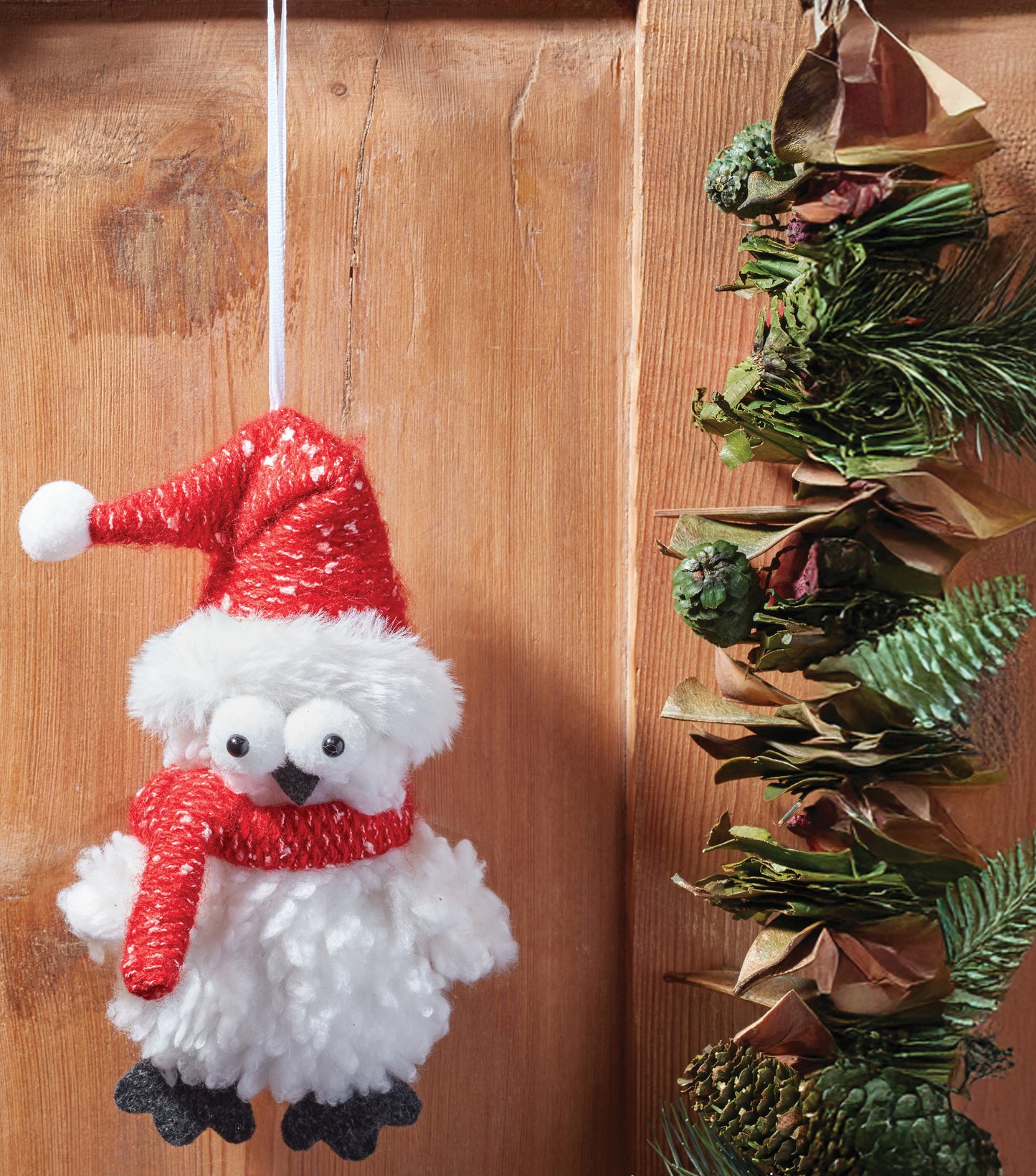 Decorative snowman ornament with a red hat and scarf hanging on a wooden surface.