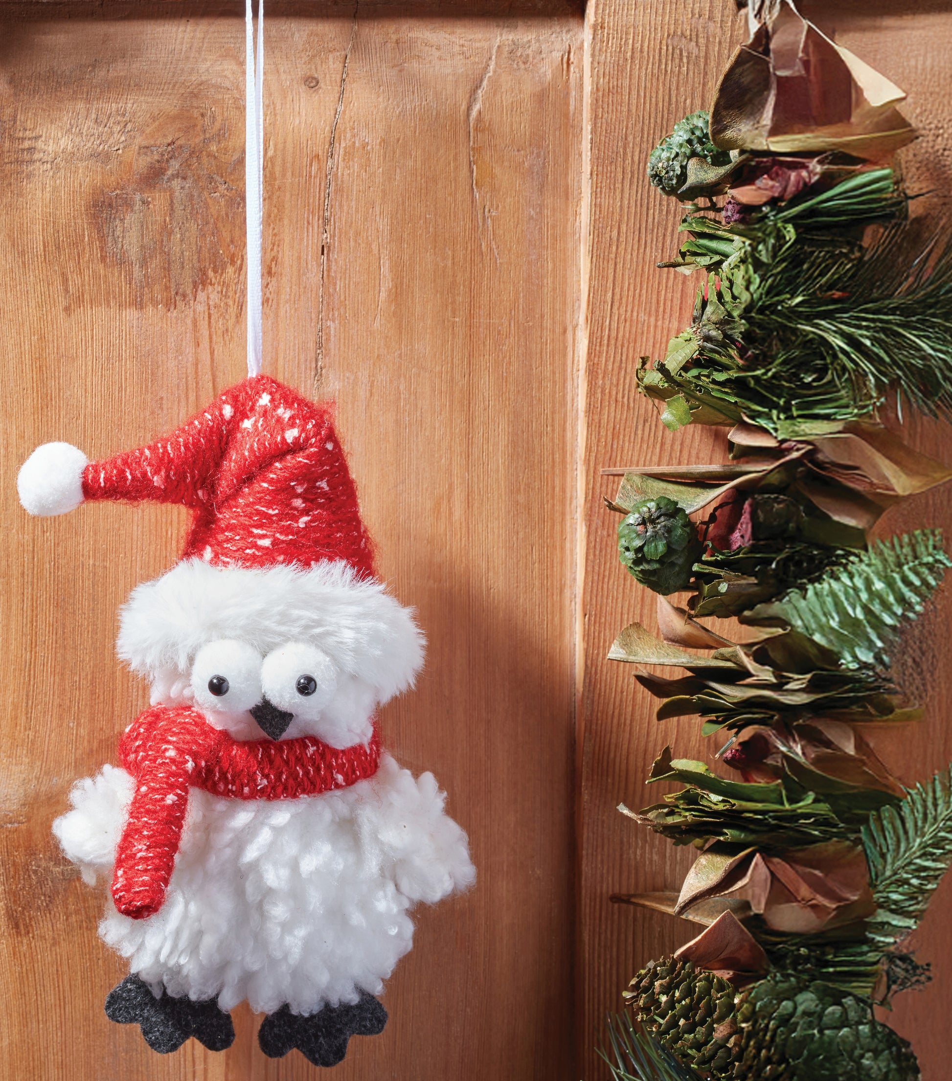 Decorative snowman ornament with a red hat and scarf hanging on a wooden surface.