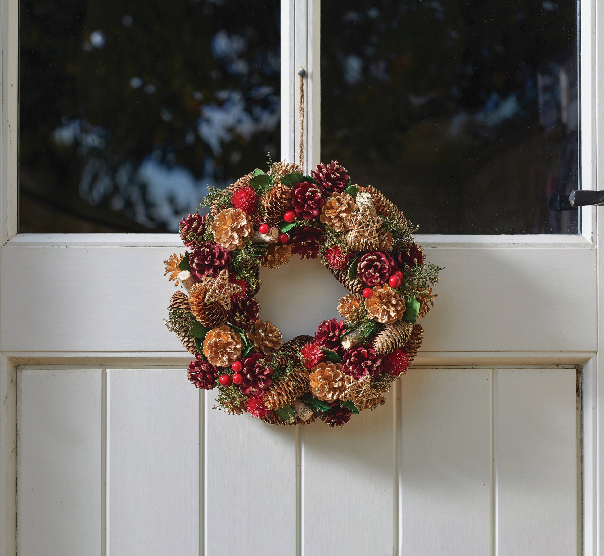 Decorative wreath with pinecones and flowers on a white door