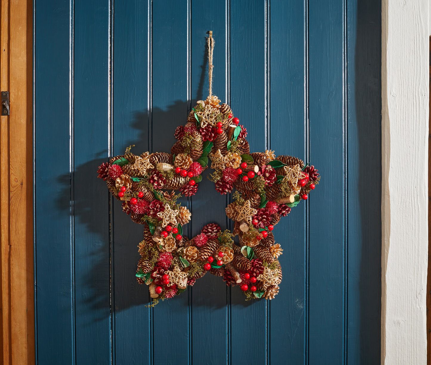Decorative star-shaped wreath with pinecones and berries hanging on a blue wooden door.