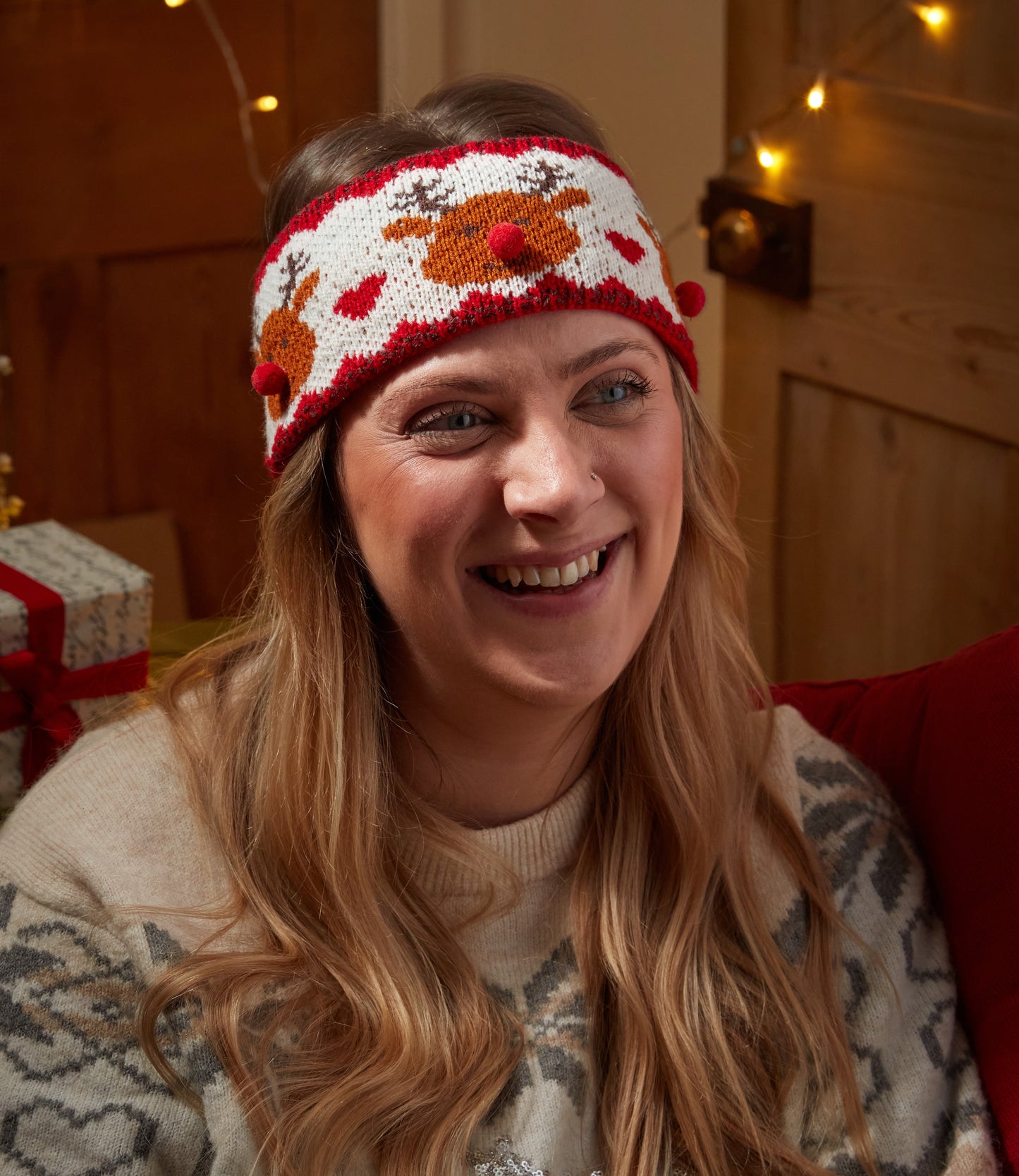 Woman wearing a festive headband with reindeer design in a cozy indoor setting.