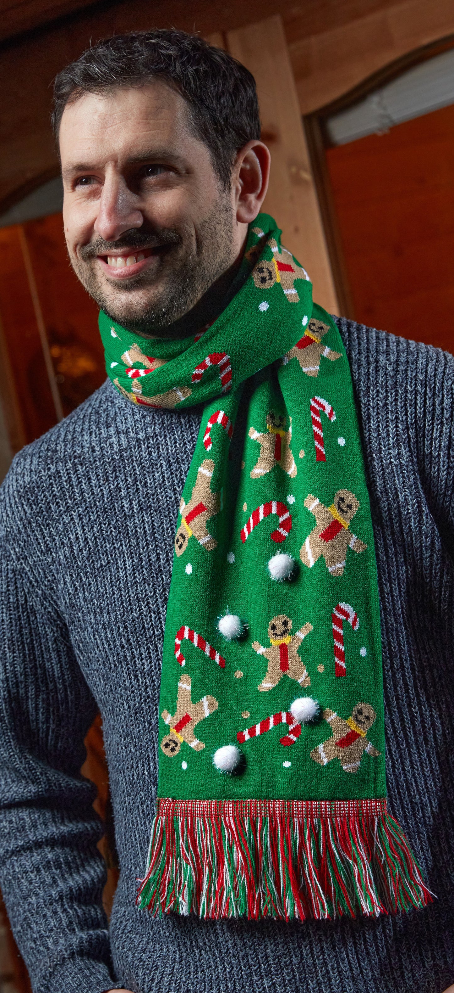 Man wearing a festive green scarf with gingerbread men and candy cane patterns.