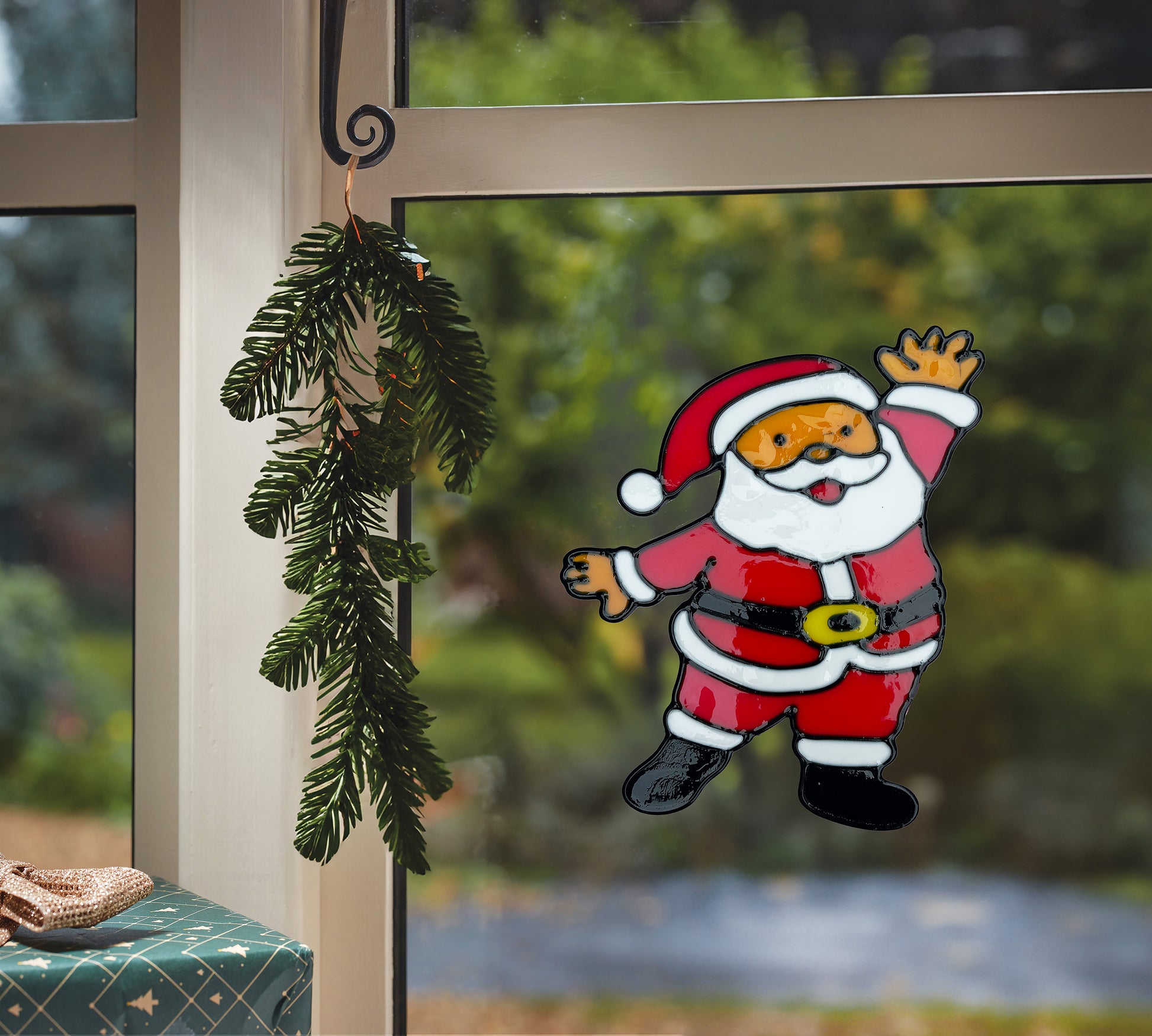 Decorative Santa Claus window cling on a glass door with greenery.