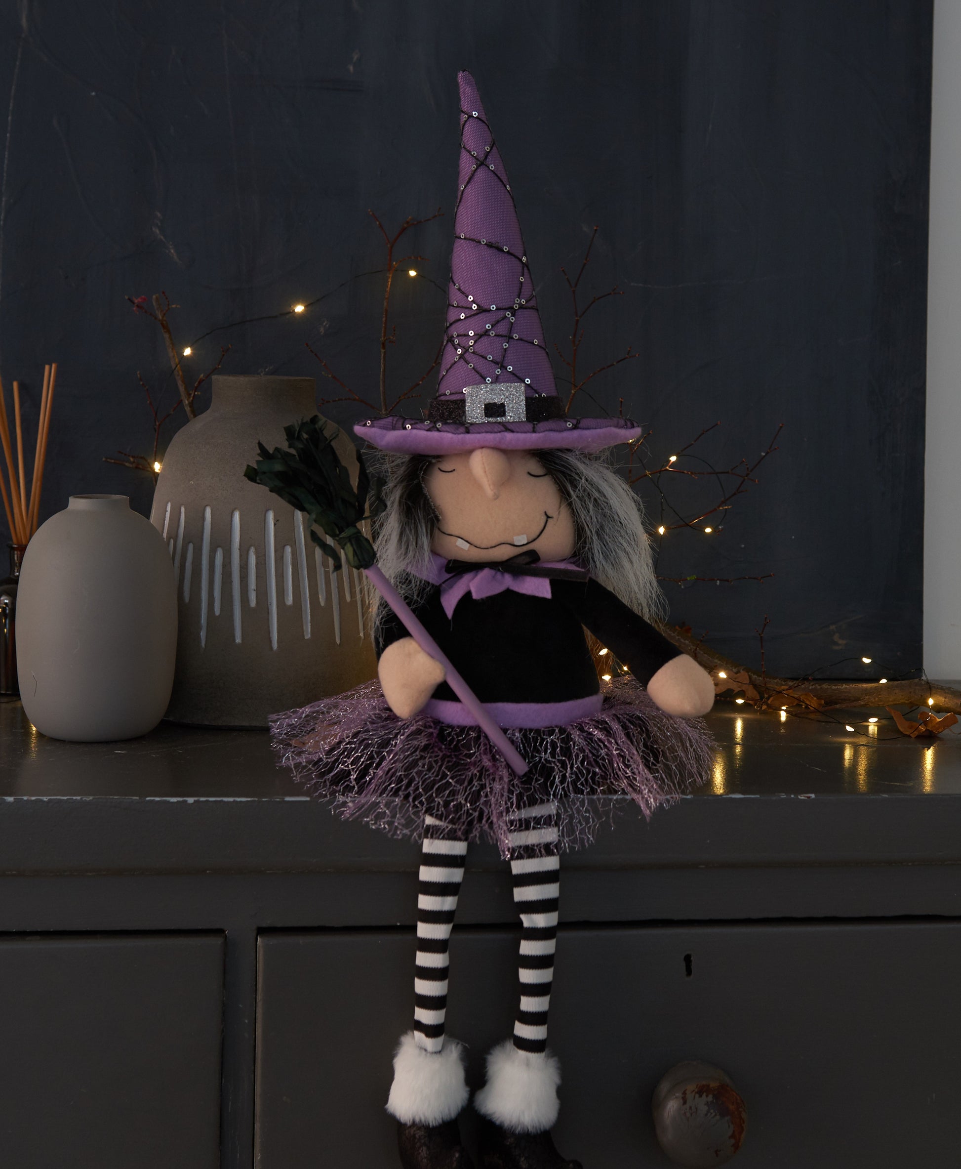 Halloween-themed doll with purple witch hat and black and white striped socks on a dark background.