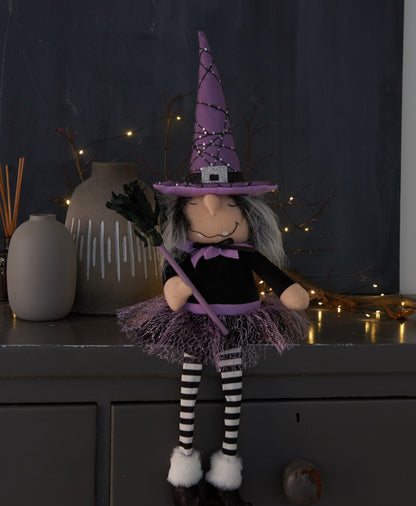 Halloween-themed doll with purple witch hat and black and white striped socks on a dark background.