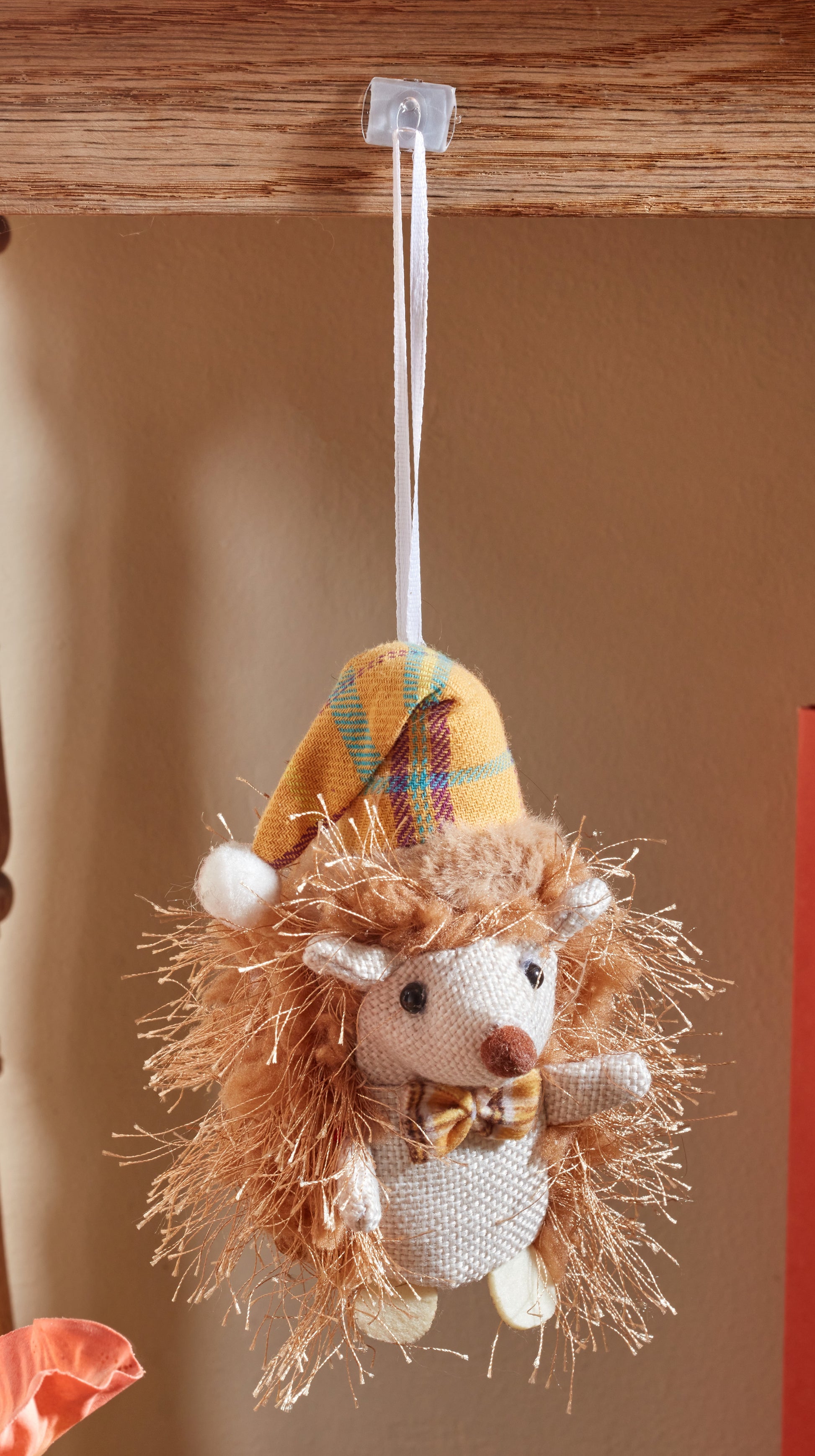 Hedgehog plush toy with a plaid hat hanging on a wooden surface.