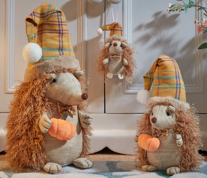 Three plush hedgehogs with plaid hats and pumpkin patches on a wooden floor.