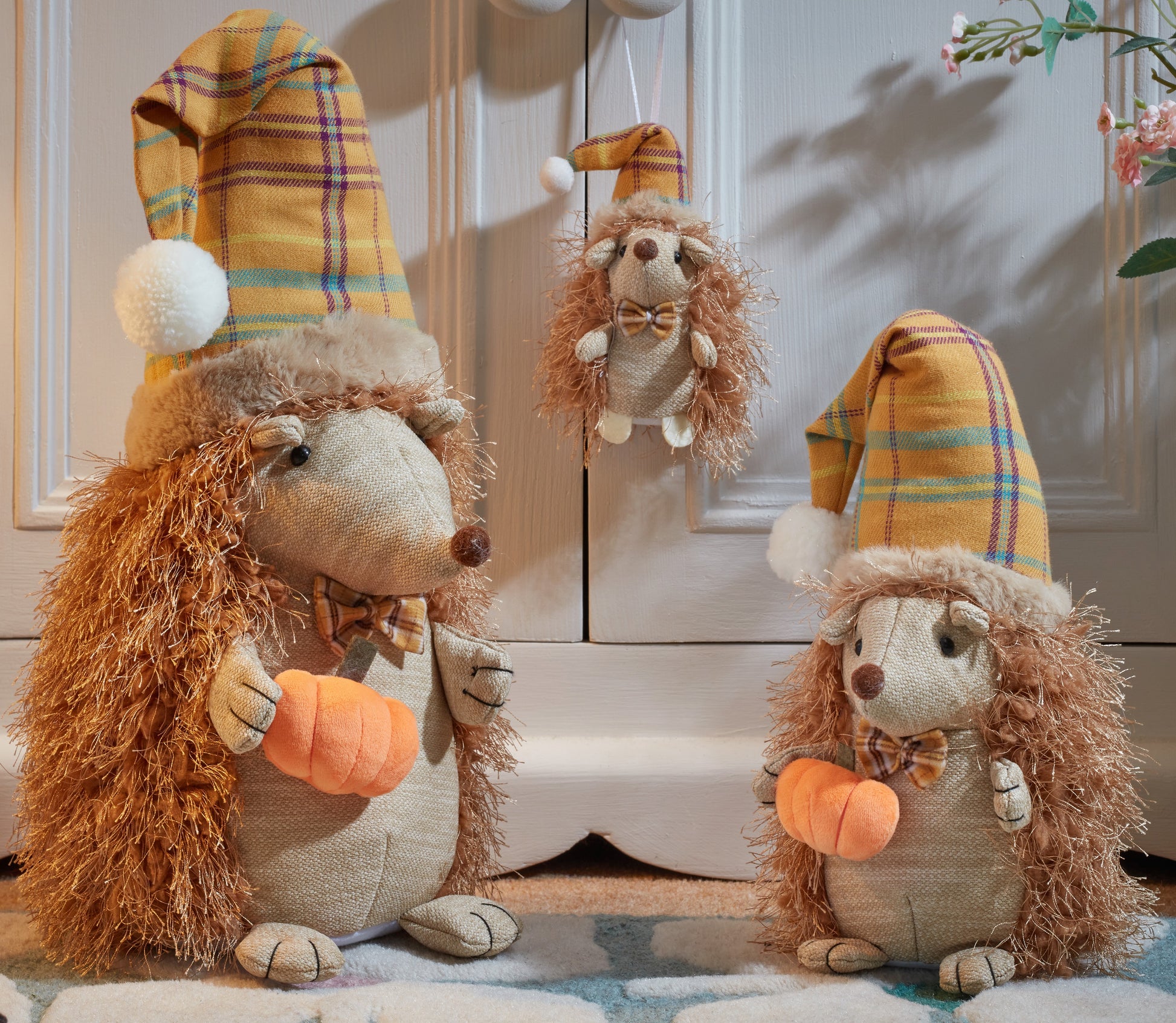 Three plush hedgehogs with plaid hats and carrot toys on a wooden floor.