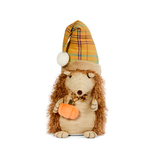 Plush toy hedgehog wearing a plaid hat and holding a pumpkin on a white background