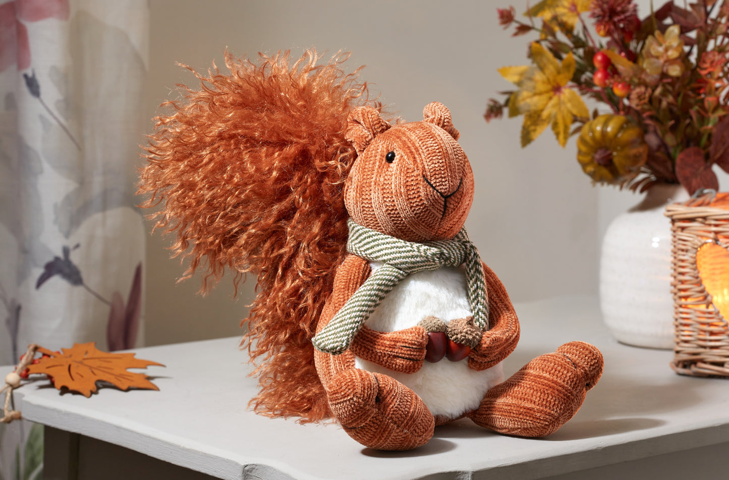 Plush squirrel toy with a scarf on a table with autumn decorations.