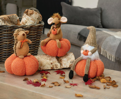 Knitted pumpkins with animal figurines on a wooden surface with autumn leaves.