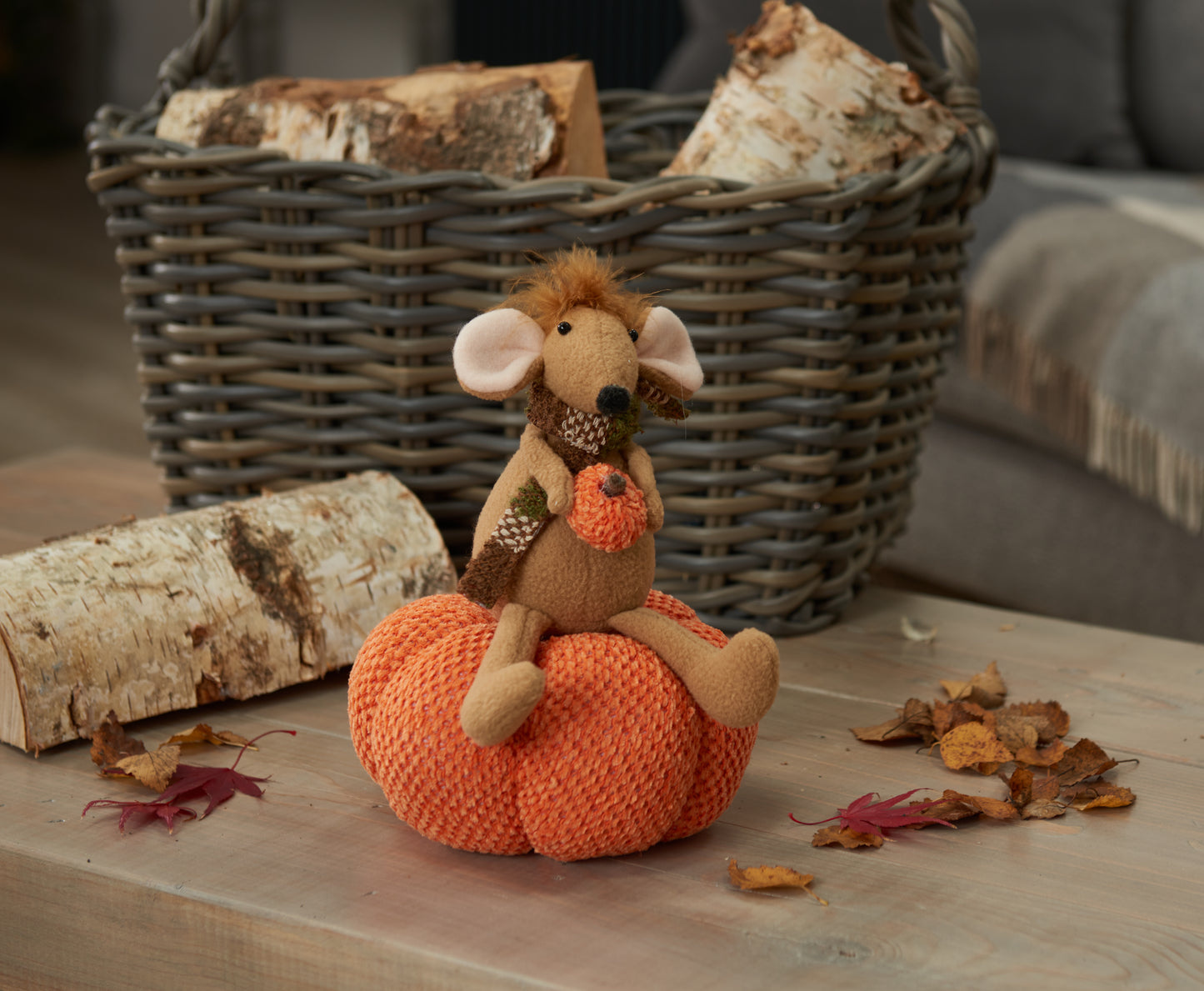 Toy mouse on an orange pumpkin with a basket and logs in the background