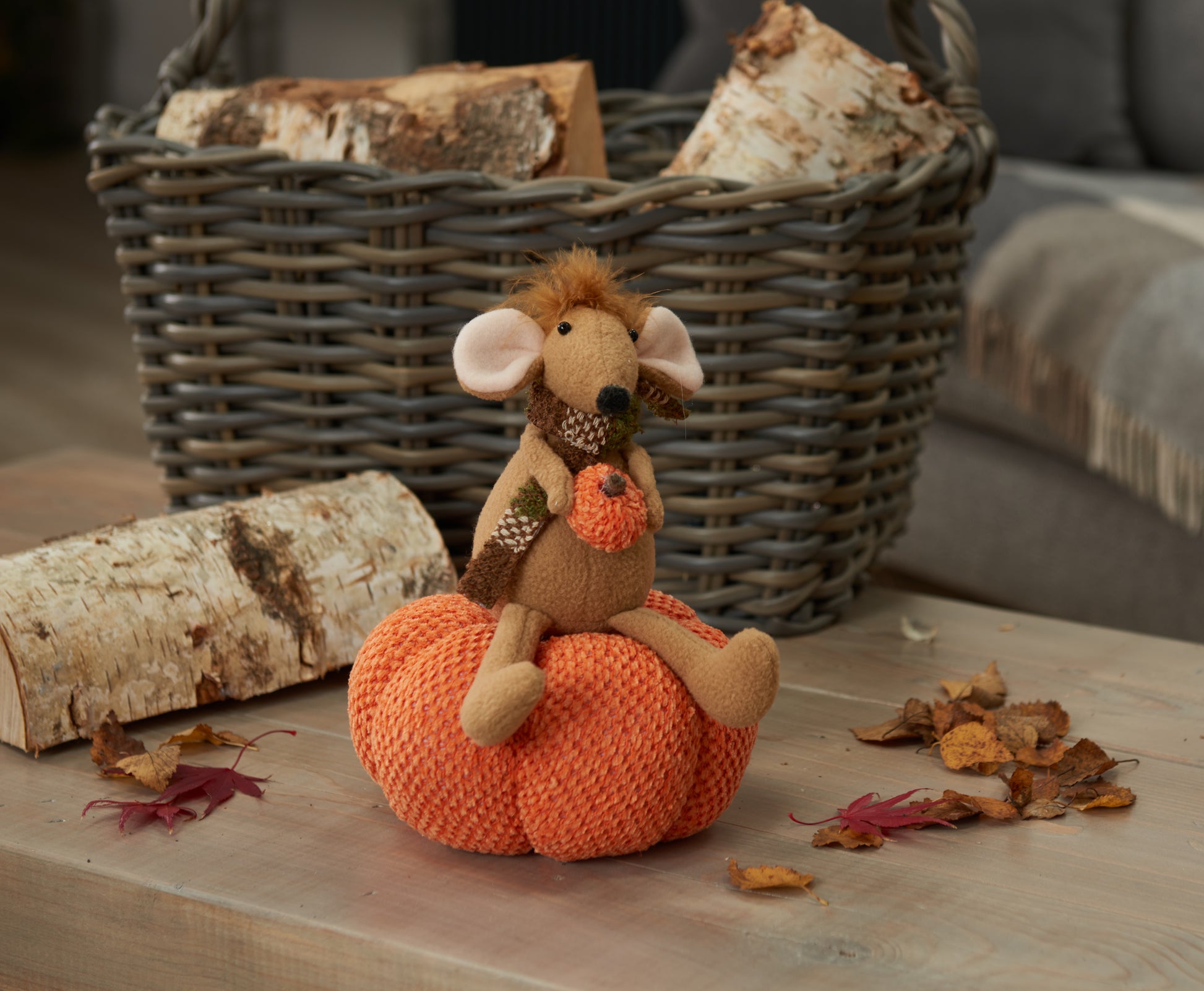 Toy mouse on an orange pumpkin with a basket and logs in the background