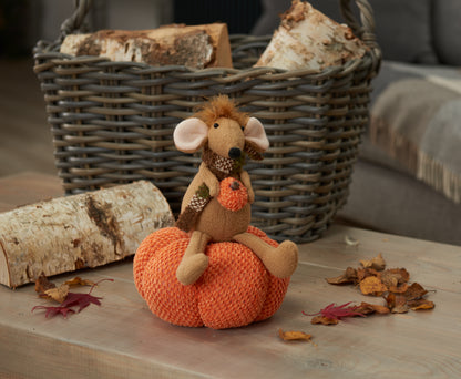 Toy mouse on an orange pumpkin with a basket and logs in the background