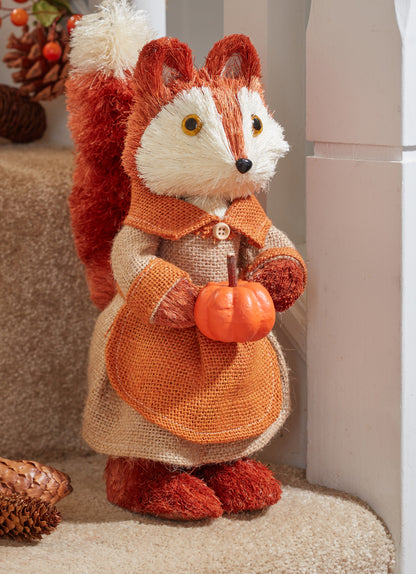 Stuffed fox toy holding a pumpkin with autumn decorations in the background