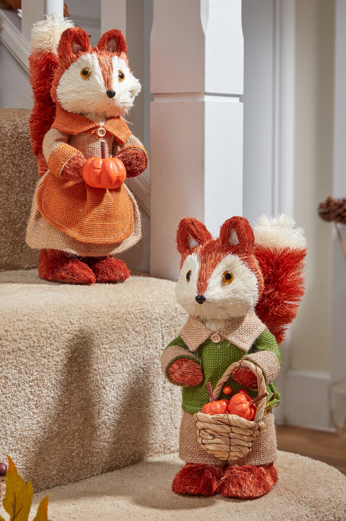Two fox figurines, one holding a pumpkin and the other with a basket of apples, on a staircase.