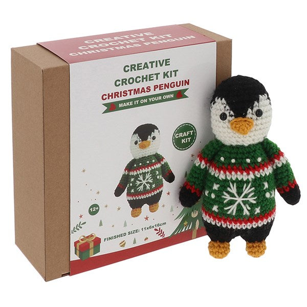 Crocheted penguin toy in a sweater next to its packaging box.