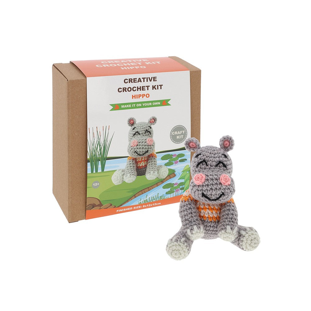 Crocheted hippo toy with a cardboard box labeled 'Creative Crochet Kit Hippo' on a white background.