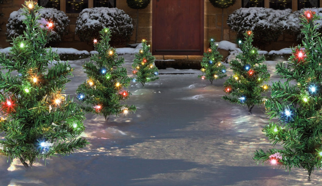 Decorative Christmas trees with lights on a snowy ground in front of a building.