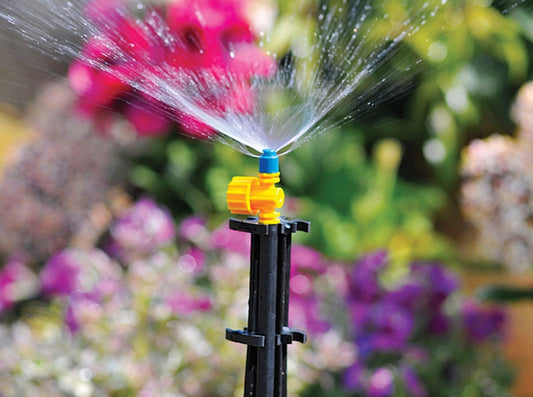 Sprinkler spraying water in a garden with flowers in the background