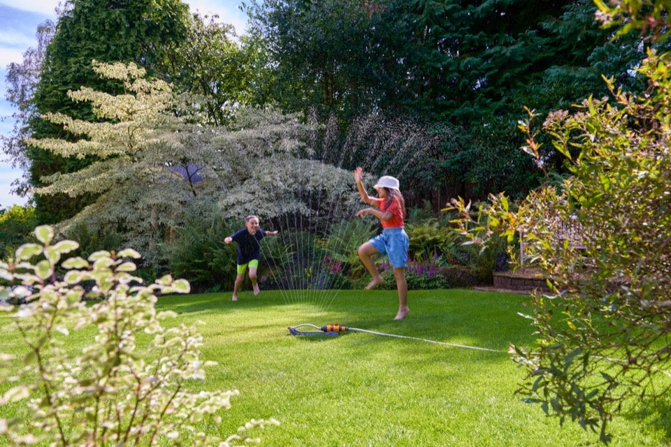 Two people playing with a sprinkler in a garden