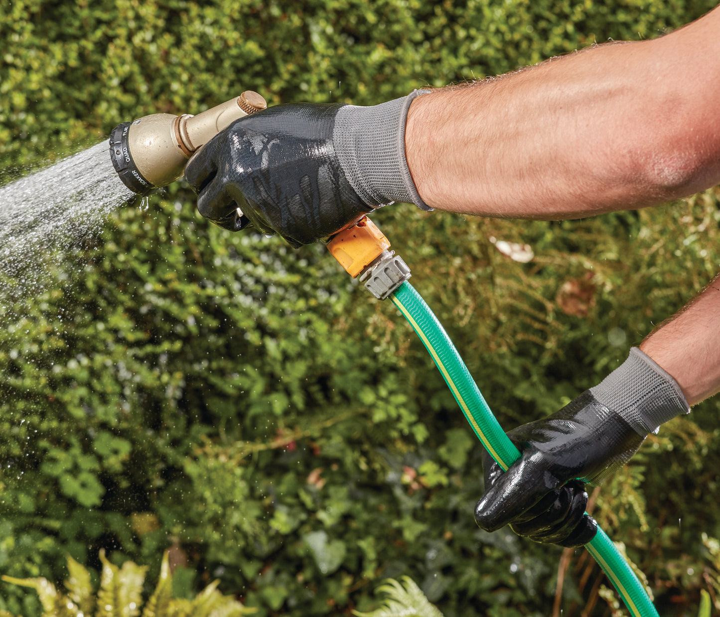 Person watering plants with a green hose against a green background