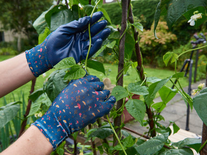 Person wearing blue gardening gloves tending to plants in a garden