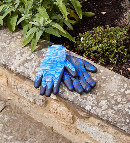 Pair of blue gardening gloves on a stone surface with plants in the background