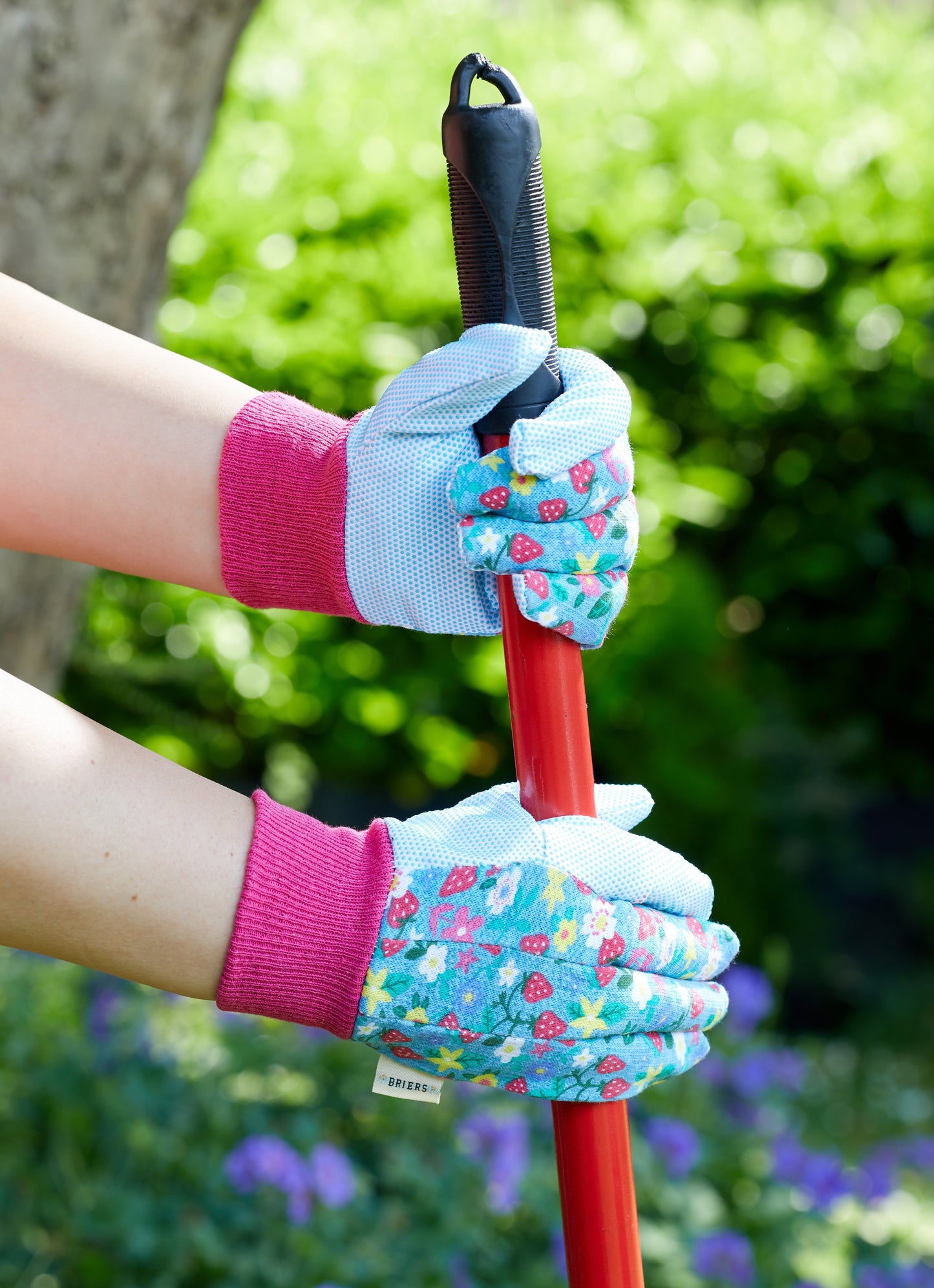 Person wearing floral gardening gloves holding a tool with a blurred green background