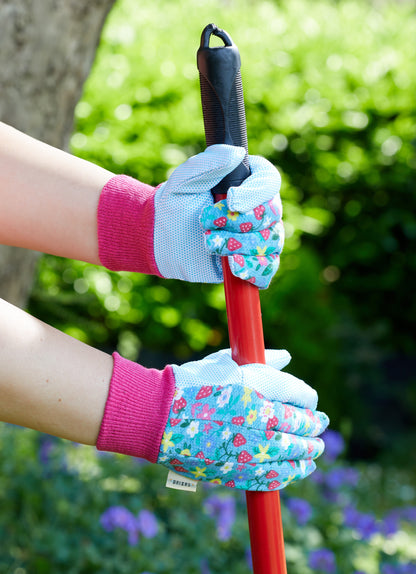 Person wearing floral gardening gloves holding a tool with a blurred green background