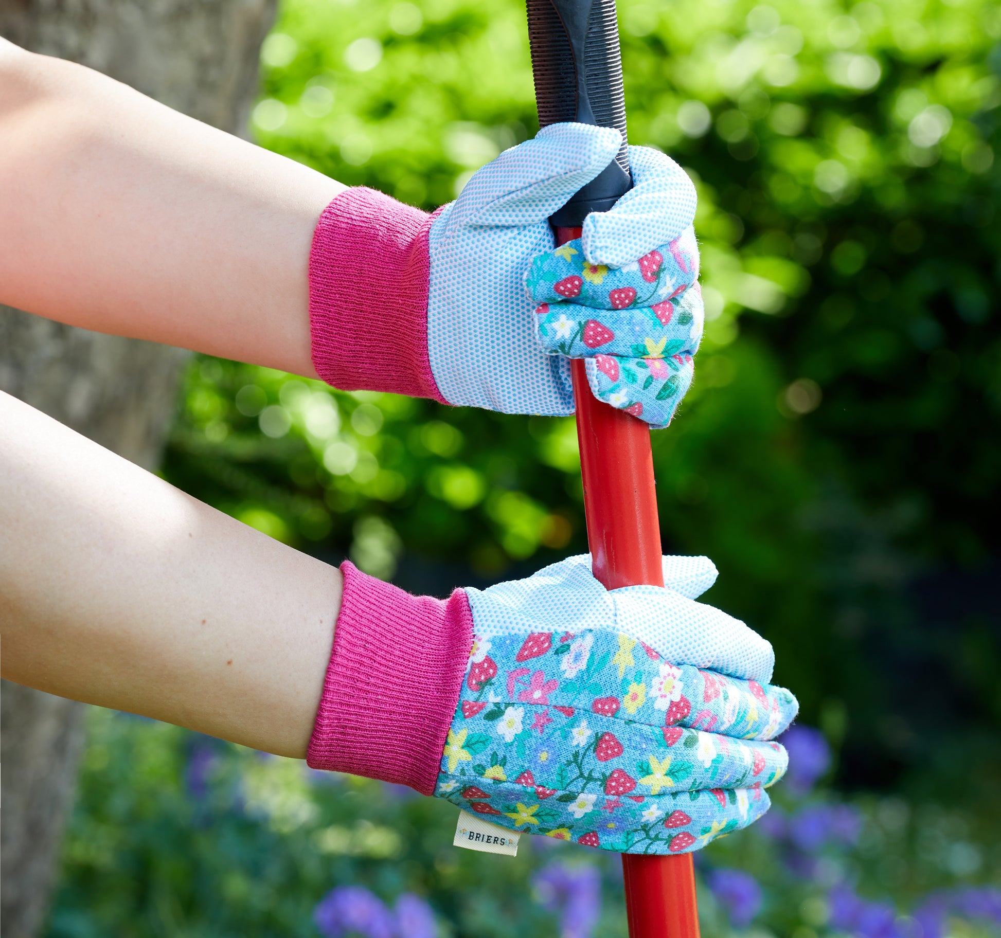 Person wearing gardening gloves holding a tool with a blurred green background