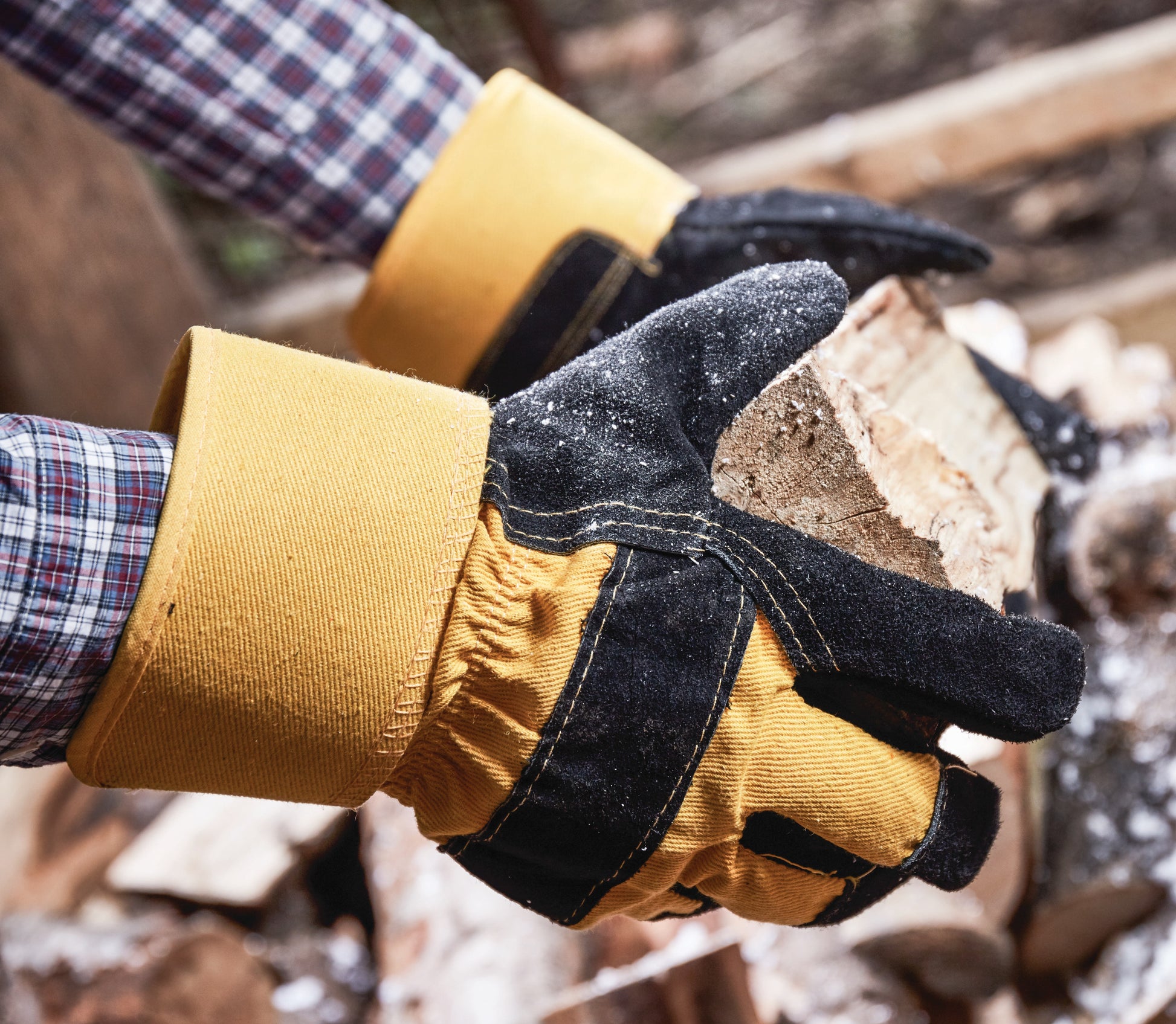 Hand wearing a yellow glove holding a piece of wood with a blurred background