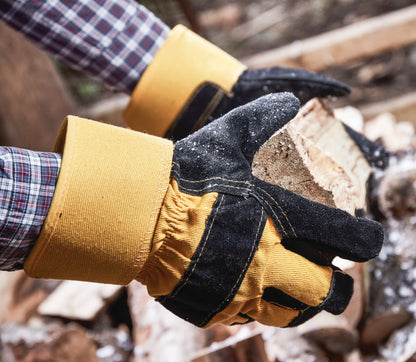 Hand wearing a yellow glove holding a piece of wood with a blurred background