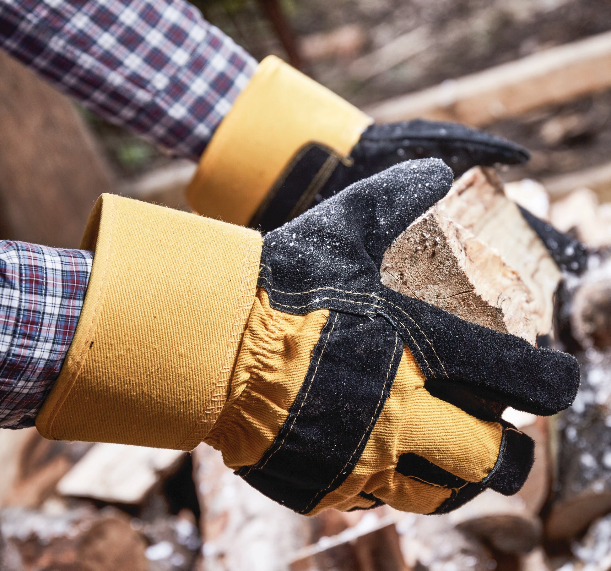 Close-up of hands wearing yellow and black gloves holding a piece of wood.