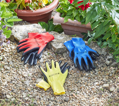 Three pairs of gardening gloves in red, blue, and yellow on a stone surface with plants in the background.