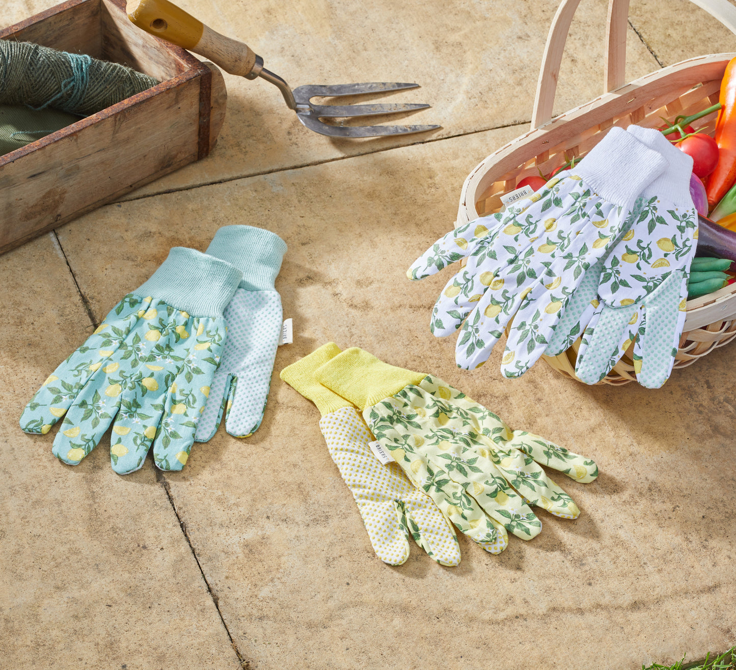 Gardening gloves with floral patterns on a stone surface with a basket of vegetables.