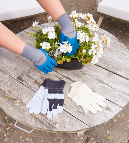 Person wearing gardening gloves with a potted plant on a wooden table
