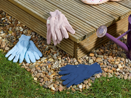 Three pairs of gardening gloves on a pebbled garden path next to a wooden deck.