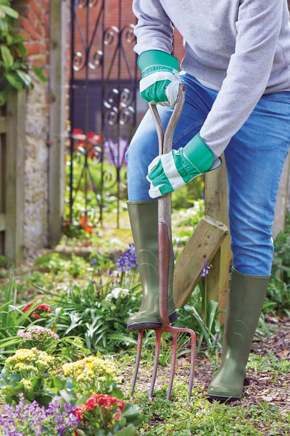 Person wearing green welling boots, digging with a garden fork