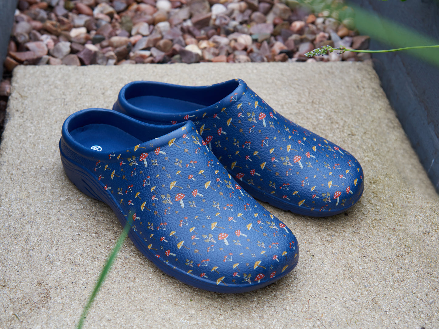 Pair of blue floral-patterned clogs on a concrete surface with a stone background