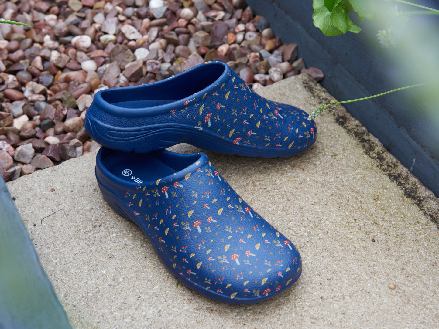 Pair of blue clogs with floral pattern on a concrete surface with pebbles in the background