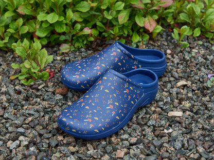 Blue floral-patterned clogs on a gravel surface with green plants.